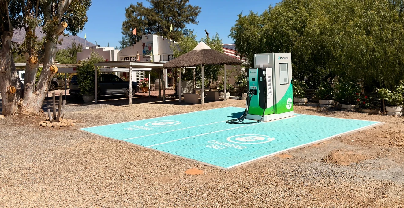 The SAEV Charge station at Die Veldskoen Padstal, De Doorns: the charger and battery cabinet at the head of two paved bays marked Charging only, with the padstal and mountains behind